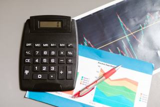 Calculatrice et stylo posés sur des graphiques financiers pour suivre la trésorerie de l’entreprise